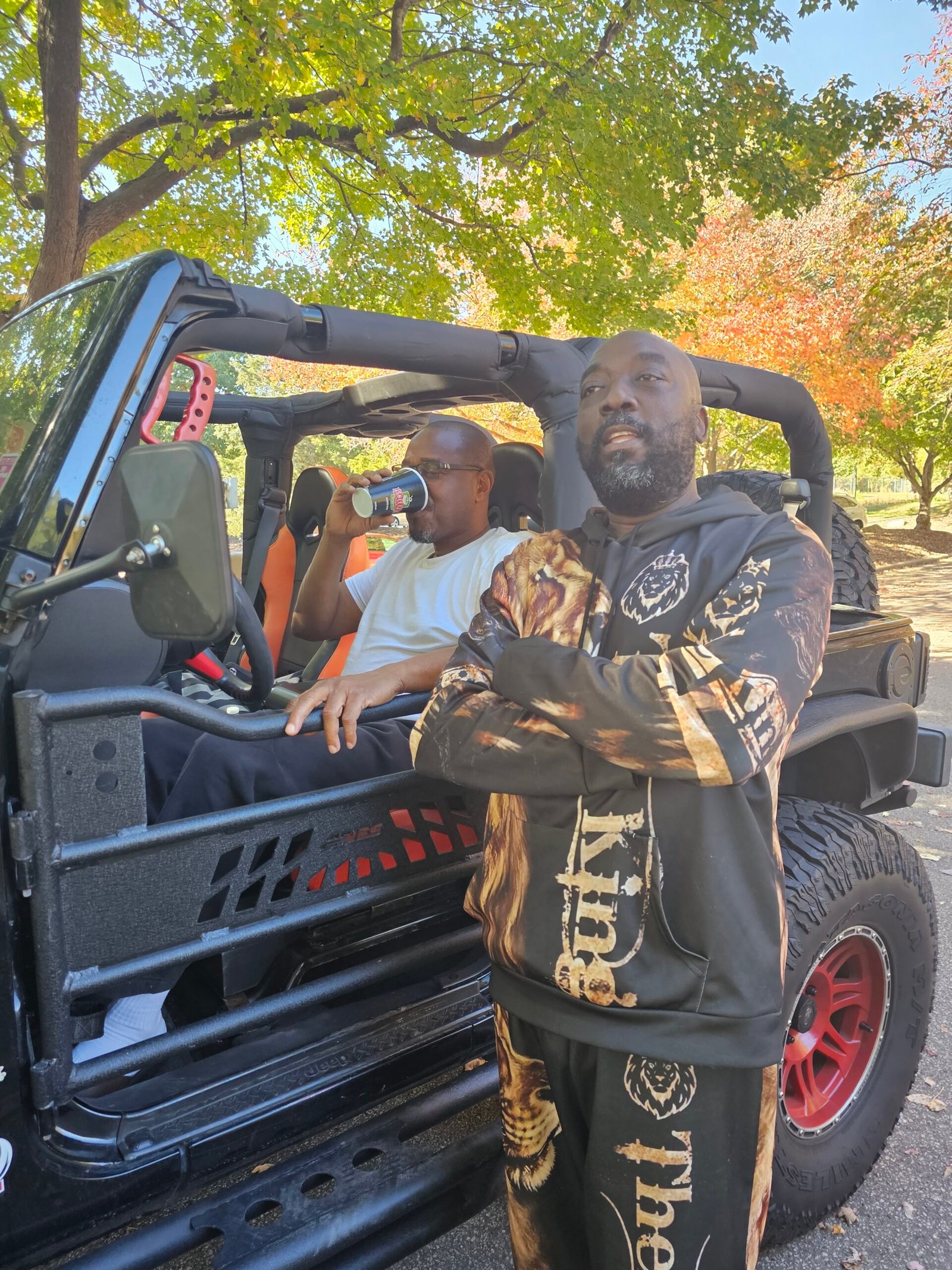 Two friends beside a Jeep beneath autumn trees